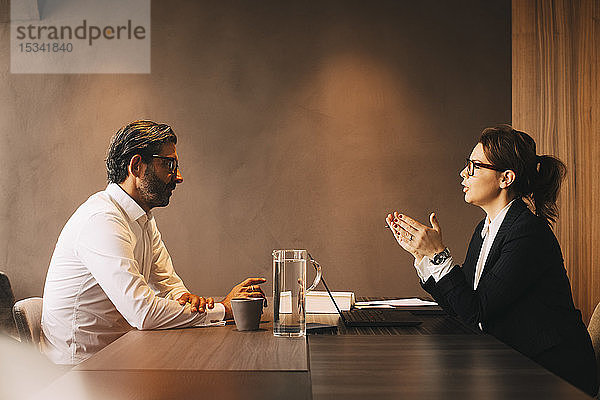 Seitenansicht einer Anwältin  die bei einer Besprechung im Büro ihren reifen Mandanten erklärt