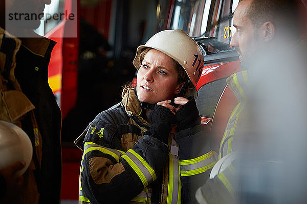 Helmtragende Feuerwehrfrau im Gespräch mit anderen Mitarbeitern der Feuerwache