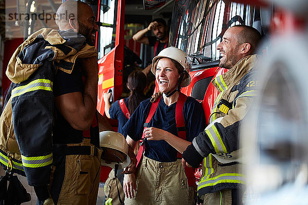 Fröhliche Feuerwehrleute unterhalten sich  während sie in der Feuerwache gegen ein Feuerwehrauto stehen
