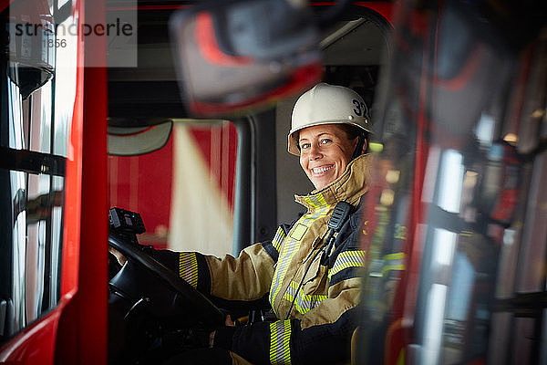 Porträt einer lächelnden Feuerwehrfrau  die im Feuerwehrauto der Feuerwache sitzt