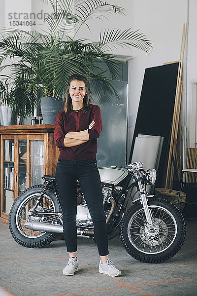 Porträt einer selbstbewussten Unternehmerin  die sich im Kreativbüro gegen das Motorrad stellt