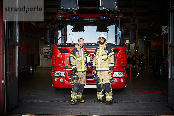 Porträt von Feuerwehrleuten  die in der Feuerwache vor dem Löschfahrzeug stehen