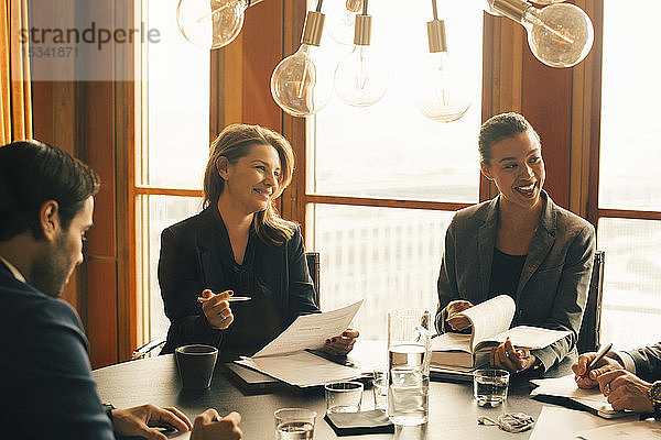 Lächelnde männliche und weibliche Rechtsexperten diskutieren bei einem Treffen im Büro über Dokumente