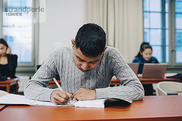 Teenager schreibt auf Buch  während er in der High School am Schreibtisch lernt