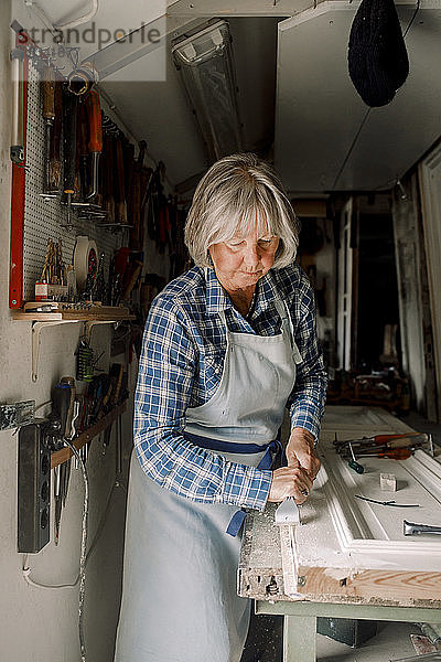 Senior-Unternehmerin kratzt in Ladenwerkstatt an Fensterrahmen