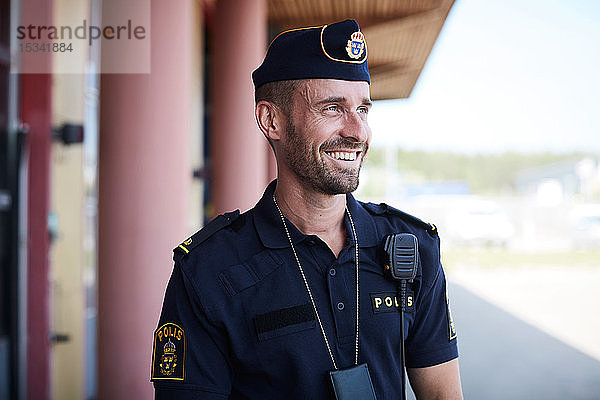 Glücklicher Polizist schaut weg  während er vor der Polizeistation steht