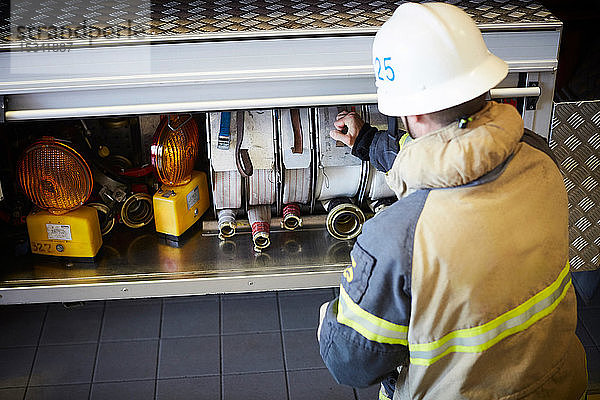 Rückansicht eines Feuerwehrmannes  der den Feuerwehrschlauch im Motor der Feuerwache anordnet