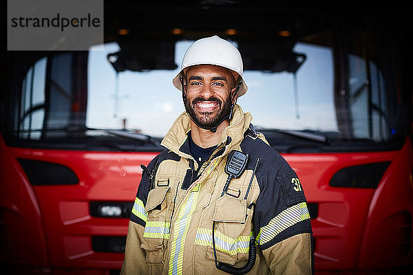 Porträt eines lächelnden Feuerwehrmannes  der vor dem Löschfahrzeug in der Feuerwache steht