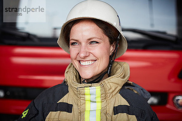 Lächelnde Feuerwehrfrau mit Helm schaut in Feuerwache weg