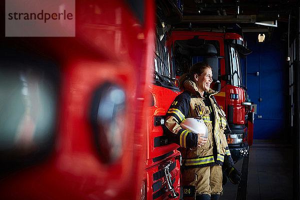 Lächelnde weibliche Feuerwehrfrau steht beim Löschfahrzeug in der Feuerwache