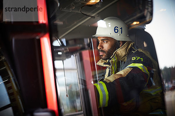 Selbstbewusster Feuerwehrmann schaut weg  während er im Feuerwehrauto sitzt