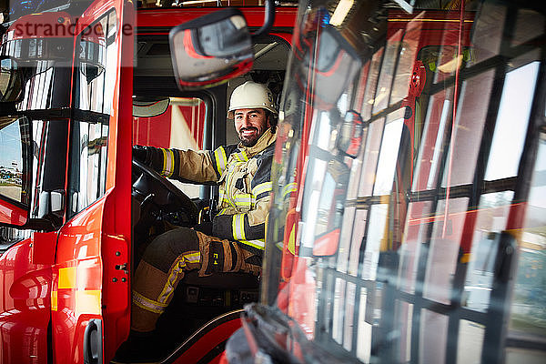 Porträt eines lächelnden männlichen Feuerwehrmannes  der im Feuerwehrauto auf der Feuerwache sitzt