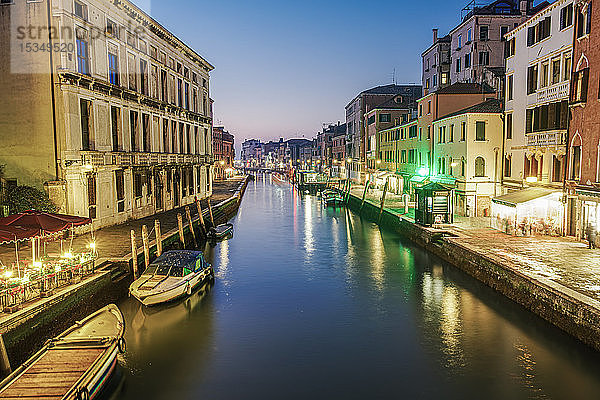 Abendlicher Kanalblick auf niedrige traditionelle Gebäude und hölzerne Kai-Pfähle mit vertäuten Booten  Venedig  UNESCO-Weltkulturerbe  Venetien  Italien  Europa