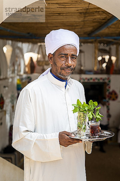 Ein ägyptischer Mann hält ein Tablett mit einem Glas Minztee und einigen frischen Minzblättern  Assuan  Ägypten  Nordafrika  Afrika