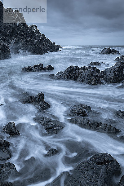 Wirbelnde Wellen über dunklen Felsen in einer zerklüfteten Bucht in North Devon  Devon  England  Vereinigtes Königreich  Europa