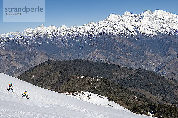 Mountainbiker radeln entlang einer schneebedeckten Piste im Himalaya mit Blick auf die Langtang-Kette in der Ferne  Nepal  Asien