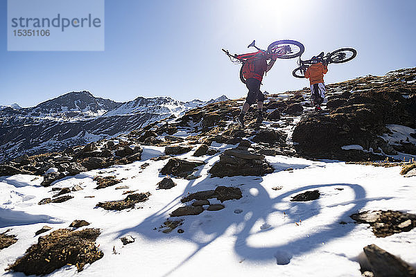 Mountainbiker tragen ihre Fahrräder einen schneebedeckten Berghang im nepalesischen Himalaya hinauf  mit Blick auf die Langtang-Bergkette  Nepal  Asien