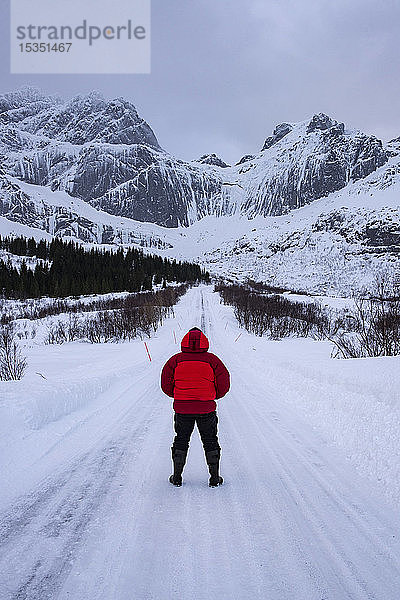 Mann auf schneebedeckter Straße in arktischen Winterbedingungen mit Bergkulisse  Lofoten  Nordland  Arktis  Norwegen  Europa