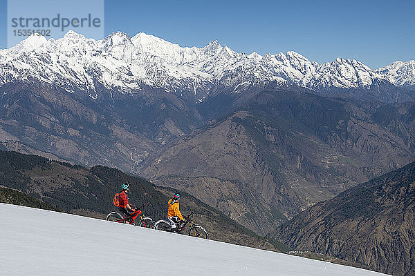 Mountainbiking auf einer schneebedeckten Piste im Himalaya mit Blick auf die Langtang-Bergkette in der Ferne  Nepal  Asien