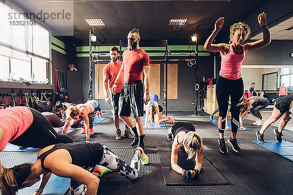 Gruppe von Frauen  die mit männlichen Trainern im Fitnessstudio trainieren und Kniebeugen machen