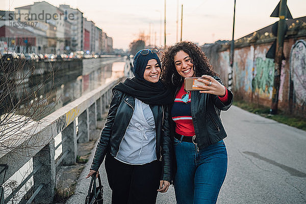 Junge Frau im Hidschab und beste Freundin beim Selfie am Stadtkanal
