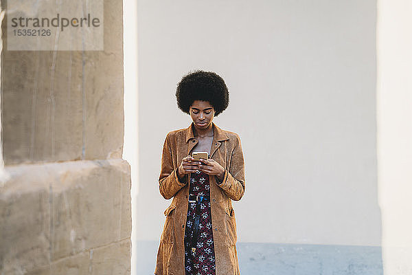 Junge Frau mit Afro-Haaren benutzt Smartphone im Korridor