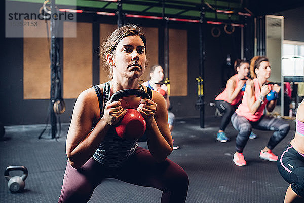 Frauen trainieren im Fitnessstudio  in der Hocke und beim Heben von Paukenglocken