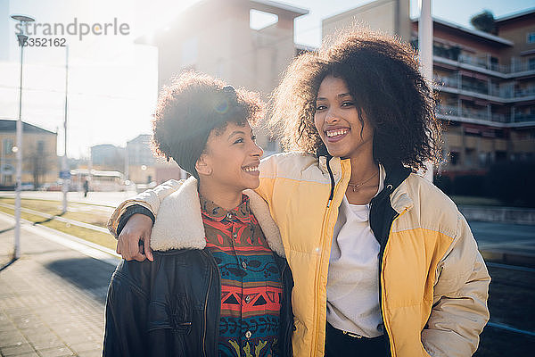 Zwei coole junge Freundinnen auf dem sonnenbeschienenen städtischen Bürgersteig  Porträt