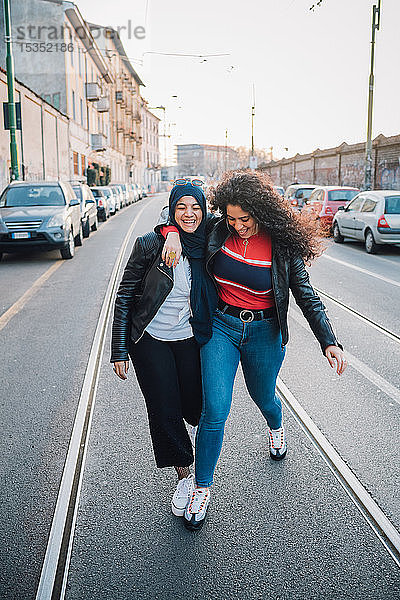 Junge Frau im Hidschab und beste Freundin überqueren Straße in der Stadt