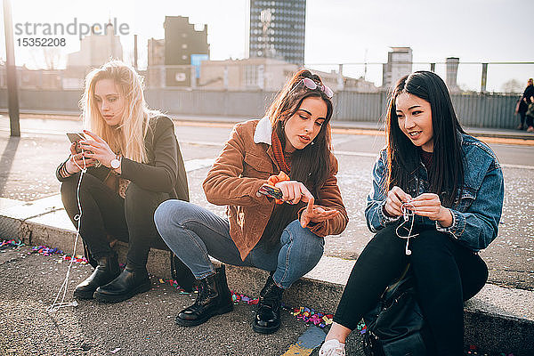 Freunde sitzen mit Smartphone am Bordstein  Mailand  Italien