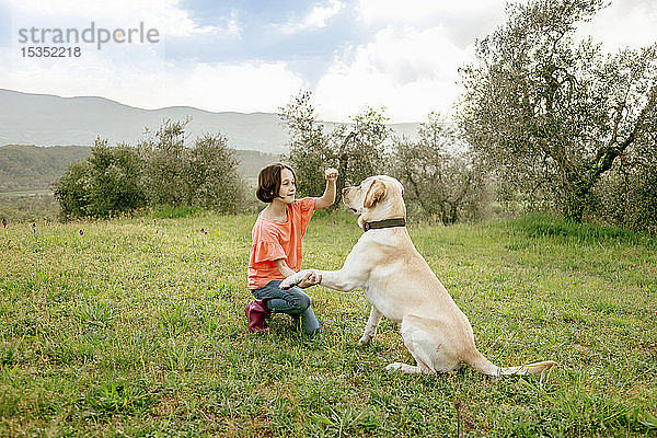 Kauerndes Mädchen spielt mit Labradorhund in malerischer Feldlandschaft  Citta della Pieve  Umbrien  Italien