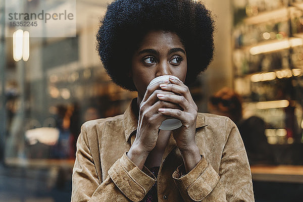 Junge Frau mit Afro-Haaren bei einem Heißgetränk vor einem Café