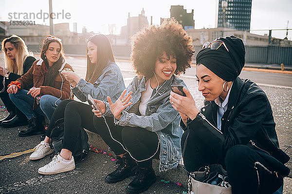 Freunde sitzen mit Smartphone am Bordstein  Mailand  Italien