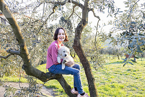 Mädchen hält einen niedlichen Golden Retriever-Welpen auf einem Baum im Obstgarten  Porträt  Scandicci  Toskana  Italien