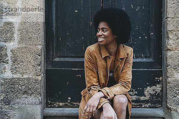 Junge Frau mit Afro-Haaren wartet an der Tür eines Steinhauses