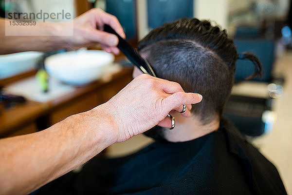 Friseur schneidet Kunden in Friseursalon die Haare