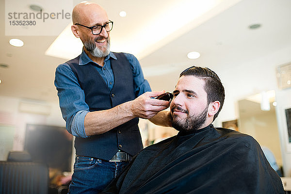 Friseur rasiert Kunden in Friseursalon