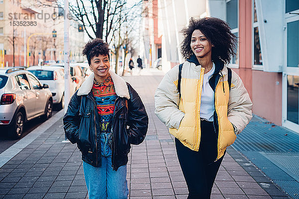 Zwei coole junge Frauen schlendern auf dem städtischen Bürgersteig