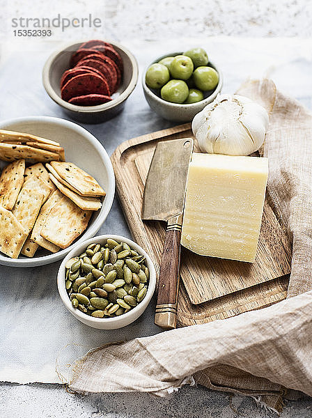 Stilleben von Schneidebrett und Käse mit Schalen mit Crackern  Oliven  Salami und Kürbiskernen  Draufsicht