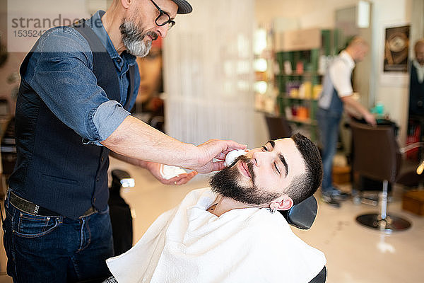 Friseur bereitet sich darauf vor  dem Kunden beim Friseur den Bart zu rasieren