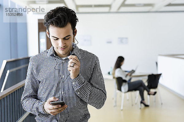 Geschäftsmann mit Smartphone im Bürokorridor  Kollege liest im Hintergrund