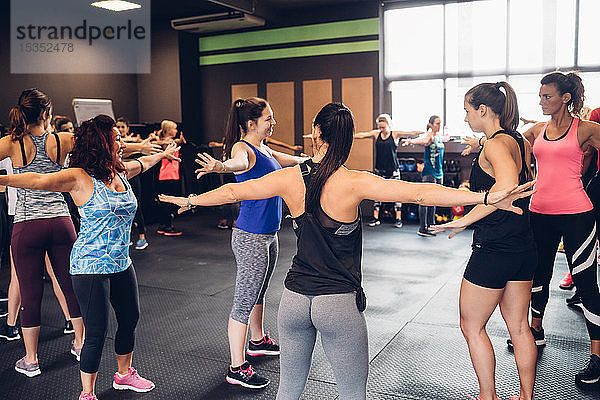 Gruppe von Frauen  die mit ausgestreckten Armen im Fitnessstudio trainieren
