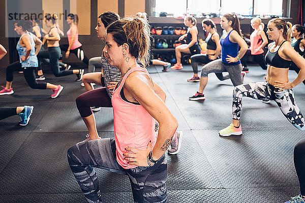 Gruppe von Frauen  die im Fitnessstudio trainieren  mit ausgestreckten Händen auf den Hüften und gestreckten Beinen