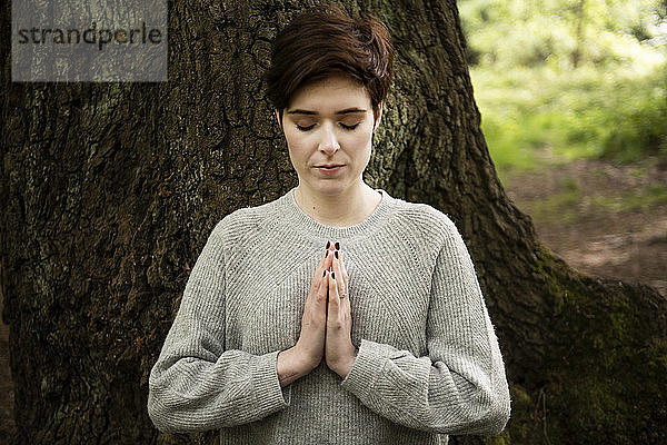 Reiki praktizierende Frau  großer Baumstamm im Hintergrund