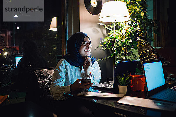 Junge Frau im Hijab an einem Café-Tisch lachend