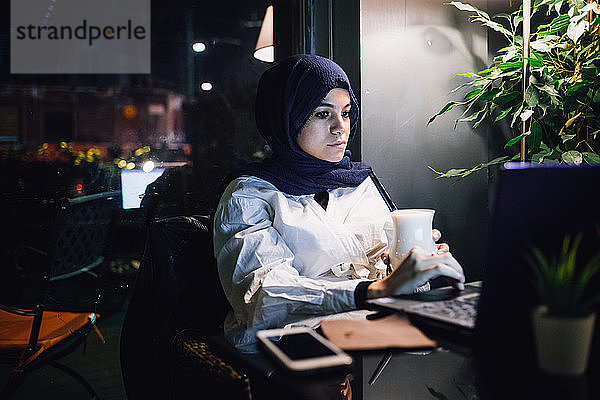 Junge Frau im Hijab betrachtet Laptop im Café