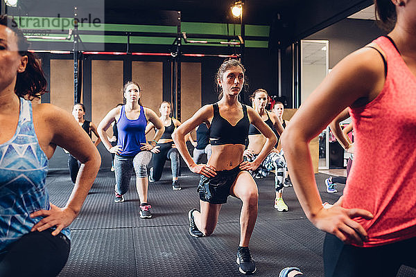 Gruppe von Frauen  die im Fitnessstudio trainieren  mit ausgestreckten Händen auf Hüften und Beinen  Vorderansicht