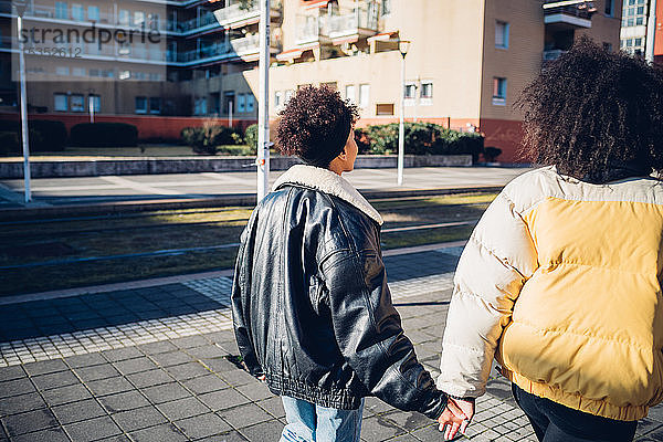 Zwei junge Freundinnen schlendern auf dem städtischen Bürgersteig  Rückansicht
