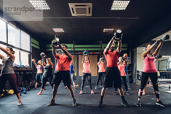 Frauen trainieren im Fitnessstudio mit männlichen Trainern und heben Kesselglocken