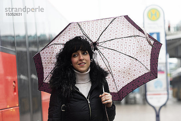 Mittlere erwachsene Frau mit Regenschirm an der städtischen Straßenbahnhaltestelle